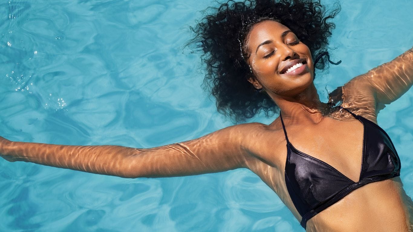 Woman with healthy curly hair swimming in pool — natural hair care routine to protect hair from chlorine damage