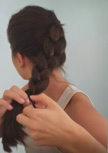 Woman securing French braid with elastic before workout — pre-workout hair styling for scalp protection