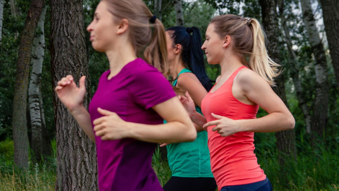 Three women running outdoors in activewear — complete hair care guide for runners
