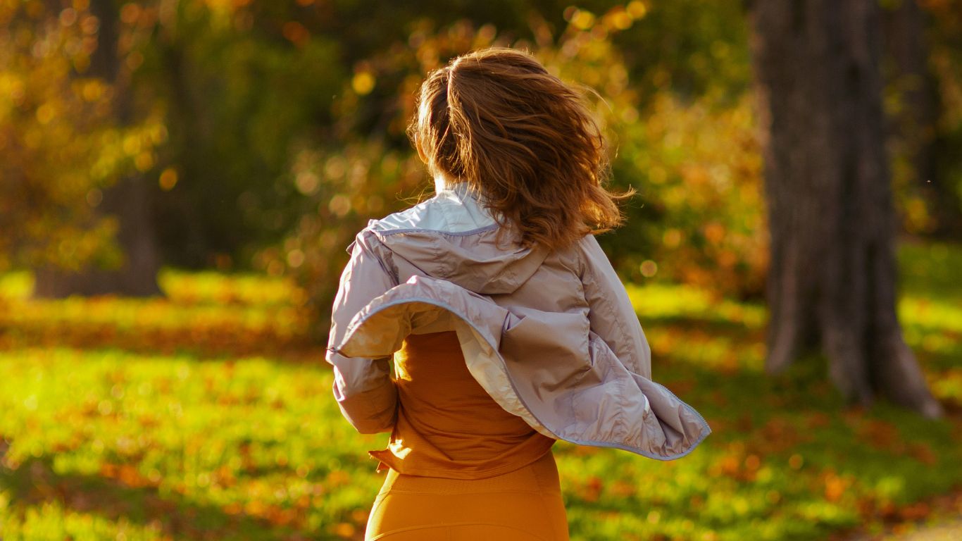 Woman in fall activewear jacket outdoors in autumn park — how cooler weather changes your hair and scalp during workouts